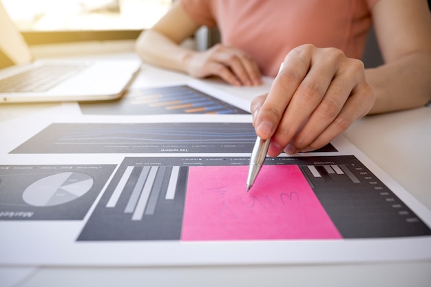 Foto asia donna mano che tiene la penna analisi il grafico con calcolatrice e laptop in ufficio a casa