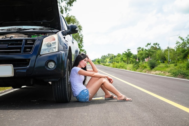 アジアの女性は彼女の車についての問題があります。美しい女性は誰かを助ける必要があります