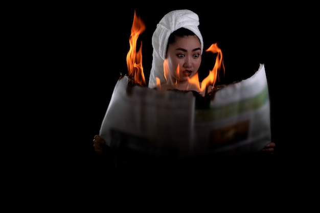 Photo asia woman is holding lit and reads a fire burning newspaper at the black background