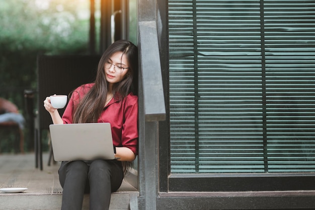 写真 アジアの女性は自宅からインターネットの仕事でパソコンとスマートフォンに取り組んでいます