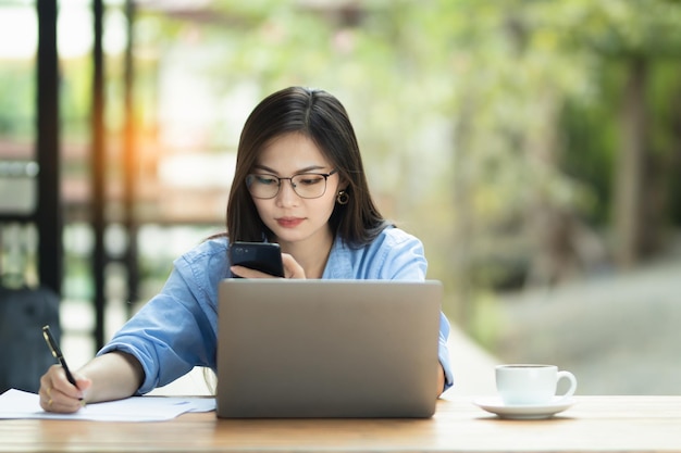 アジアの女性は自宅からインターネットの仕事でパソコンとスマートフォンに取り組んでいます