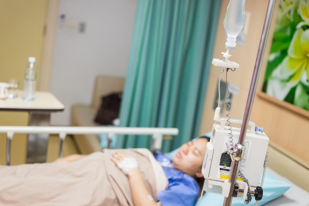 La donna dell'asia pazienta con la macchina automatica della soluzione di infusione iv nella stanza paziente