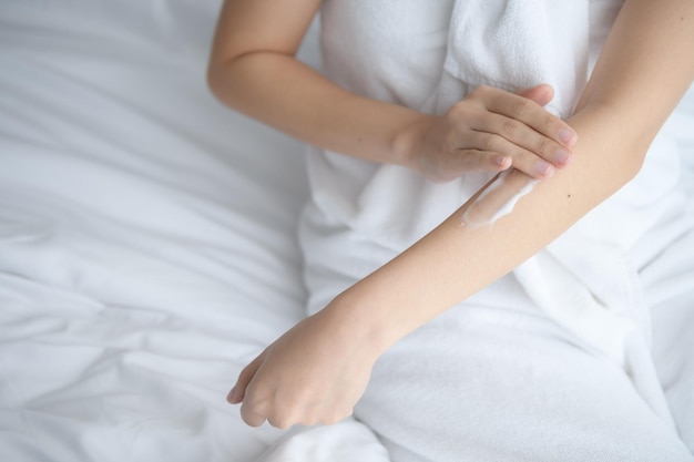 Asia woman sitting on bed and applying cream on body