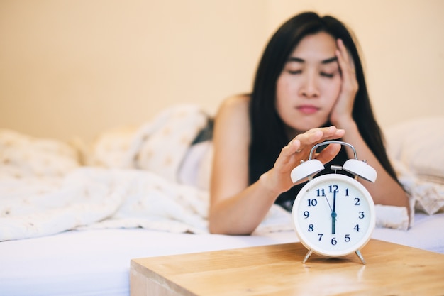 Азиатская женщина сонная не хочет вставать в 6 часов утра с помощью будильника