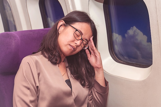 アジアの女性は飛行機の中で頭痛に苦しんで