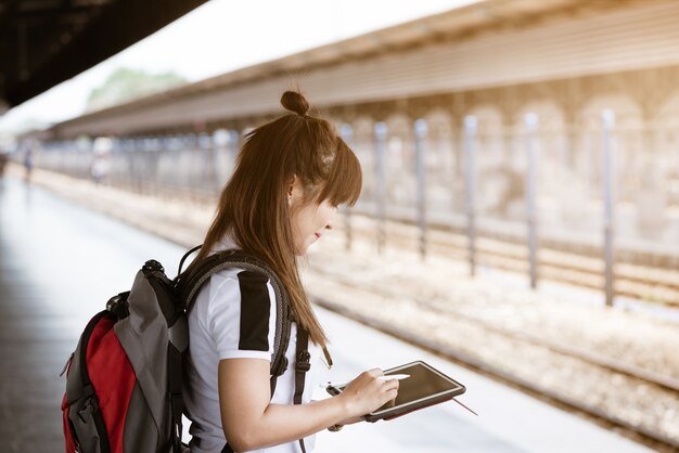 Asia woman traveler feeling happiness using smartphone while waiting for a train.