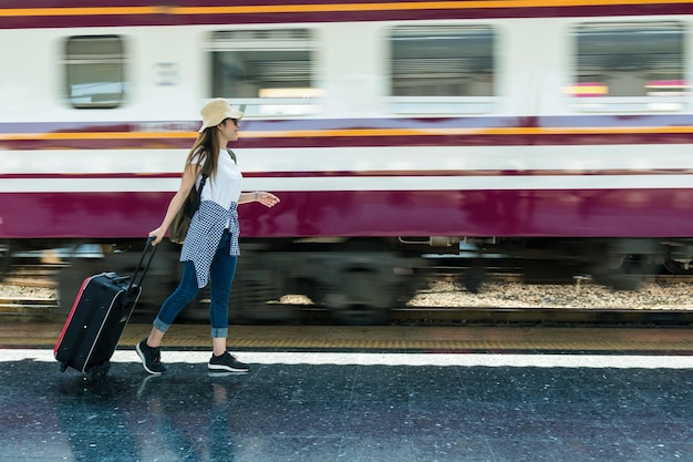 アジアの女性旅行者が歩いて、電車の走行のぼやけた動きで荷物をけん引します