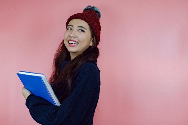 アジアの若い女の子はピンクの背景のノートブックを保持します。