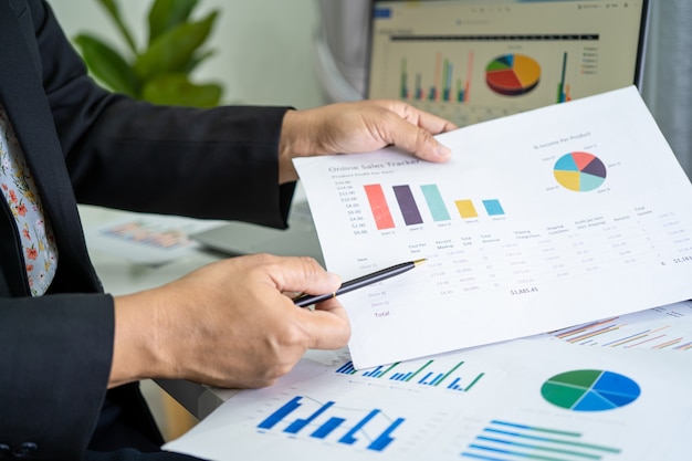 Asian accountant working and analyzing financial reports project accounting with chart graph and calculator in modern office, finance and business concept.