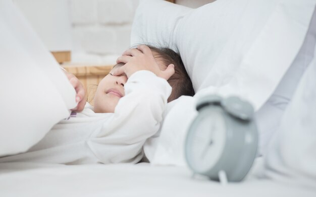 Asian adorable little girl laying on white bed cover eyes with hand lazy to wake up