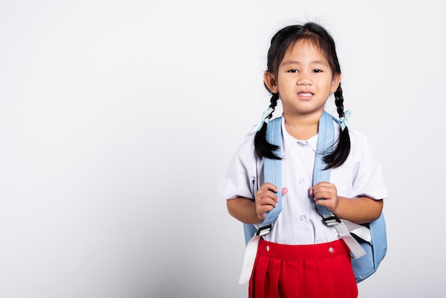 立っている学生タイの制服赤いスカートを着て幸せな笑顔のアジアの愛らしい幼児