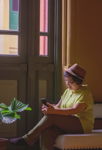 Asian adult female tourist using smartphone while relaxing on couch inside of vintage building