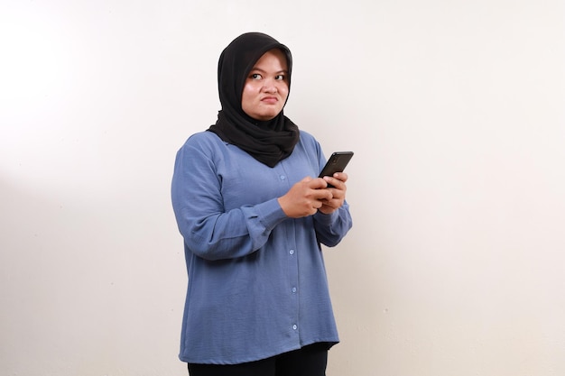 Asian adult woman standing holding a cell phone while looking sideways with unhappy face expression