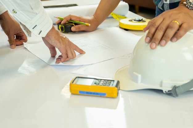 Asian architectuer working on plan hands pointing at bluepring sketch.