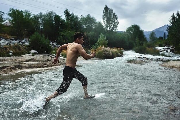 Atleta asiatico su una corsa mattutina sul fiume, pareggiatore kazako nel primo piano della natura