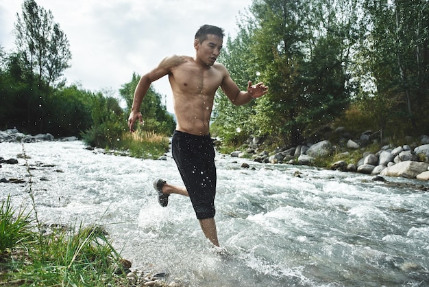 Atleta asiatico su una corsa mattutina sul fiume, pareggiatore kazako nel primo piano della natura