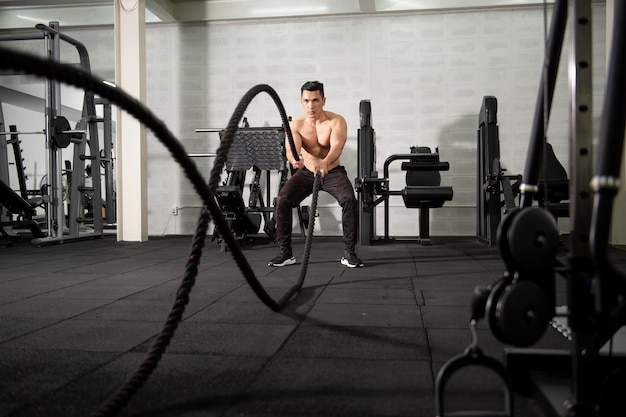 フィットネスジムで運動をしているロープを持つアジア運動男