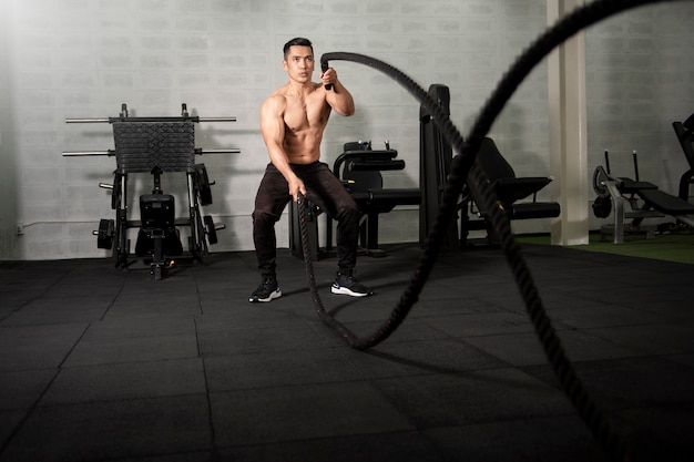 Asian athletic man with rope doing exercise in fitness gym