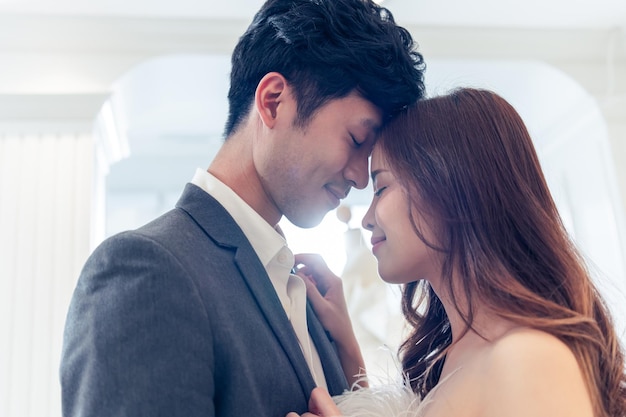 asian attractive fiance couple kissing each other in wedding studio beautiful young man and woman feel happy and relax enjoying preparation for marriage ceremony in fitting room at the bridal store