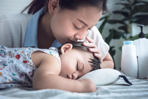 アジアの魅力的な母親は幸せと愛を込めて眠っている彼女の赤ちゃんの生まれたばかりの娘にキスしています