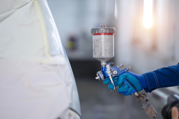 Asian auto mechanic wearing protective suit and respirator paints car body bumpers in paint roomspraying cars in paint room