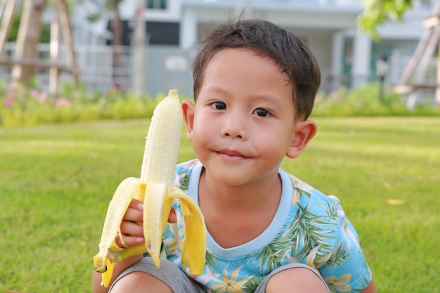 Asian baby boy age about 4 years old eating banana in the garden