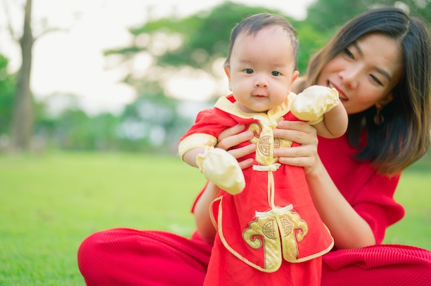 彼女の母親と一緒に中国の赤いスーツを着るアジアの赤ちゃん