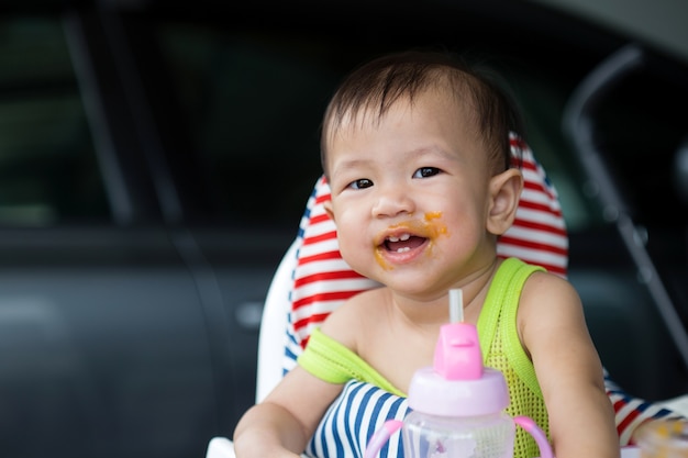 Bambino asiatico che mangia cibo sul seggiolone, età di 8 mesi