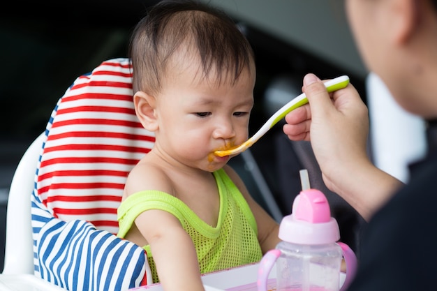 Азиатский ребенок ест пищу на высоком стуле, Возраст 8 месяцев