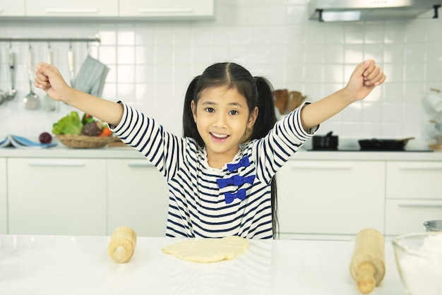 写真 アジアの女の赤ちゃんがキッチンで準備しています。面白い小さな女の子は笑顔の歯で手を上げます。