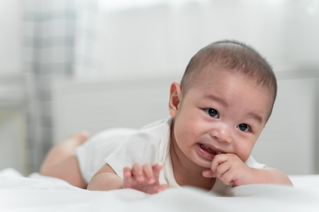 Asian baby is laughing and playing toy ball on white bed with feeling happy and cheerful