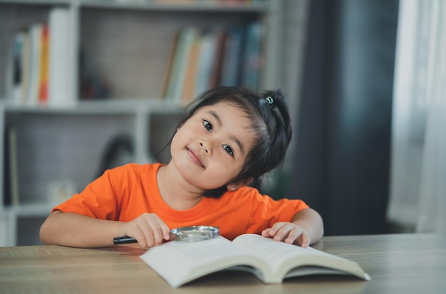 Asian baby kid girl holding magnifying glass over book and reading book education people children and school concept happy smiling student girl learning studying Education development concept