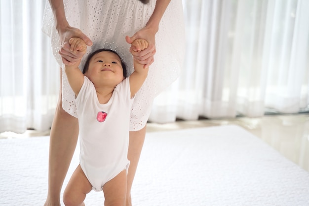 Il bambino asiatico che intraprende i primi punti cammina in avanti con il supporto della madre.