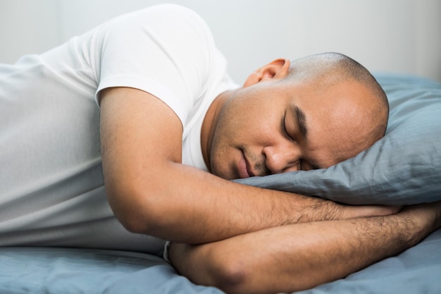 Азиатский лысый мужчина лет 30 в белой футболке спит.