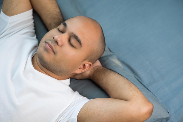 An asian bald man around the age of 30 in a white tshirt is sleeping