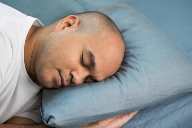 An Asian bald man around the age of 30 in a white Tshirt is sleeping