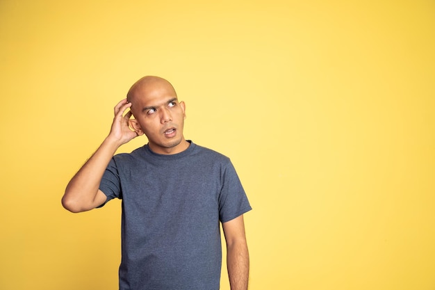 Asian bald man daydreaming while glancing up holding head