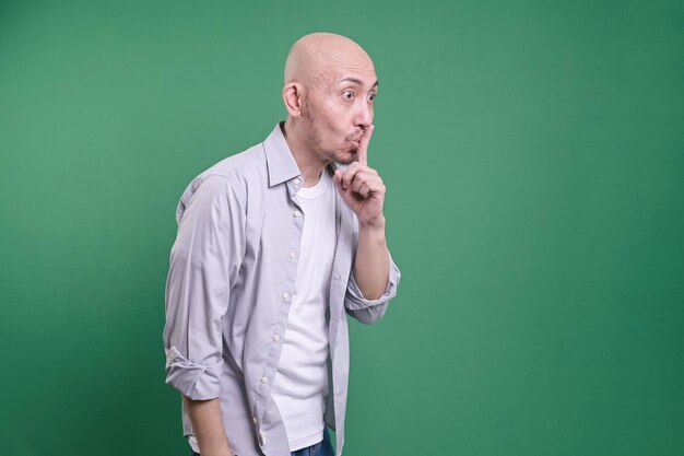 Photo asian bald man keeps finger on lips asks not tell secret information or keep silence