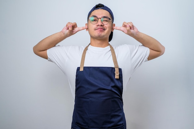 Asian barista man wearing apron cover ears with hands fingers
do not want to listen scream