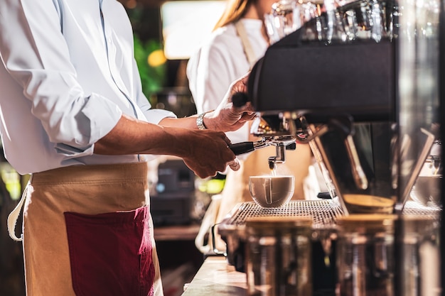 一杯のコーヒー、ラテまたはカプチーノとエスプレッソを準備するアジアのバリスタ