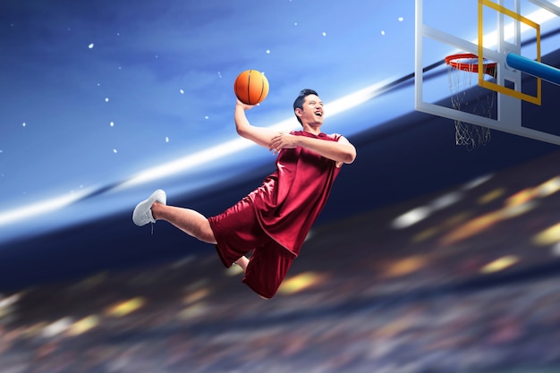 Азиатский баскетболист прыгает в воздухе с мячом, пытаясь забить