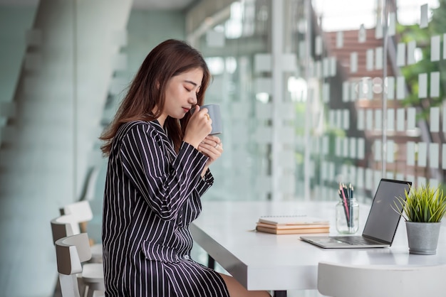 Bella donna asiatica di affari che beve caffè che si siede all'ufficio