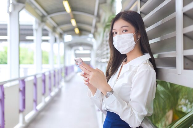 Una bella donna d'affari asiatica si trova sul cavalcavia dello skytrain in città mentre usa il suo smartphone