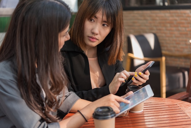 アジアの美しいビジネス女性のコーヒーカフェショップでタブレットとスマートフォンの操作