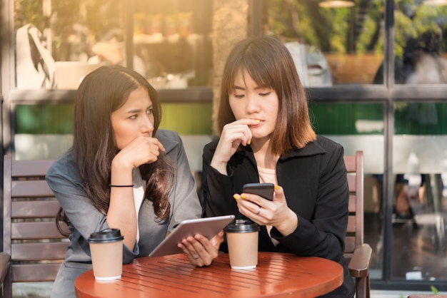 La bella donna asiatica di affari che lavora con la compressa e lo smartphone nel caffè del caffè comperano