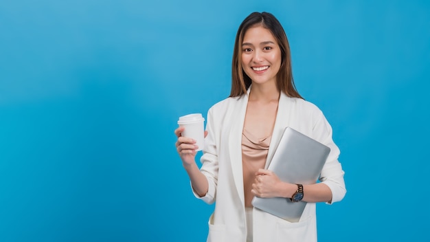 Asian beautiful businesswoman holding laptop and coffee cup in blue colour background.