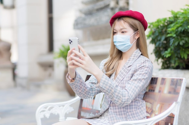 スーツと赤い帽子を身に着けているアジアの美しい女性は彼女の手でビデオ通話のためのスマートフォンを保持します