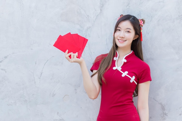 Asian beautiful girl in red dress stands and holds a red envelope with an excited expression