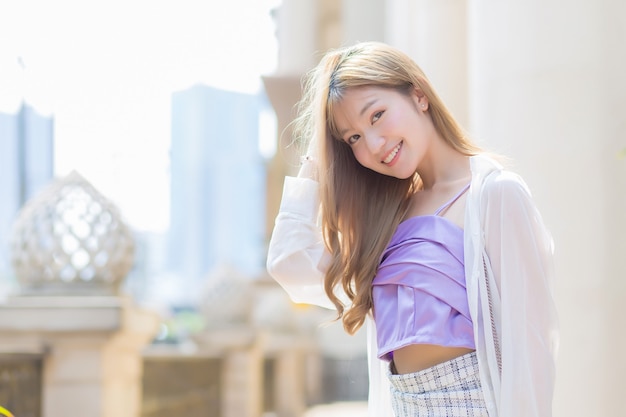 청동 머리를 한 아시아의 아름다운 소녀는 패션 스타일 테마로 미소를 짓고 거리를 걷습니다.