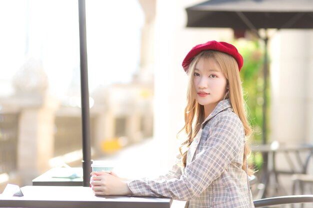 Asian beautiful girl who wears suit and red cap with bronze hair sits on chair in coffee shop